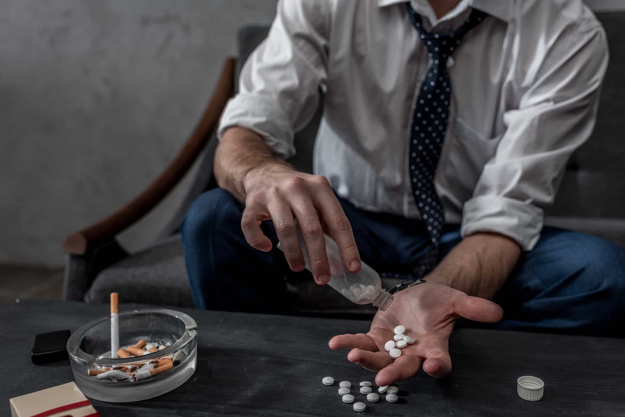 Businessman with drug addiction pours pills into his hand from bottle